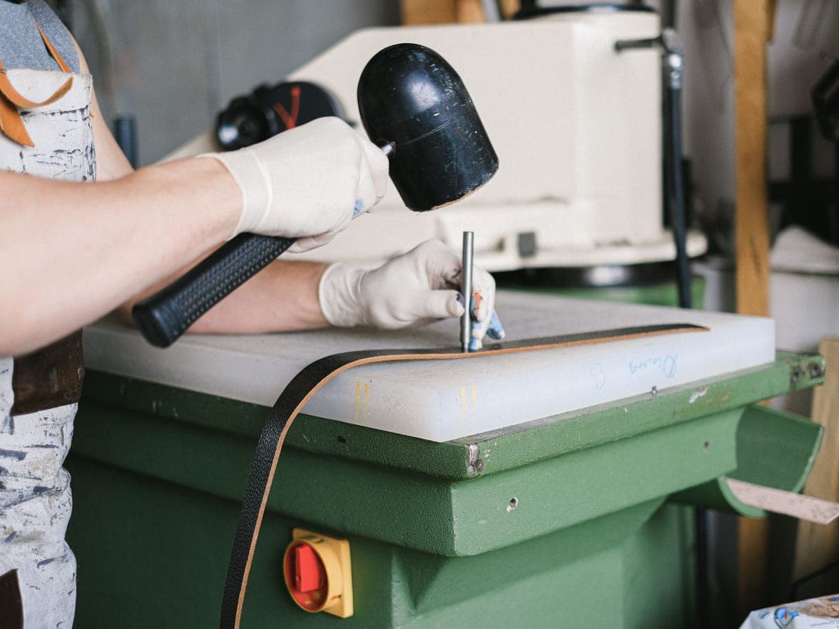 Gloved hands using a mallet and punch at a workshop bench