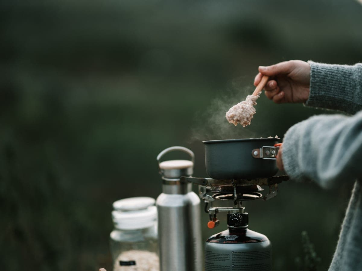 A pot boiling on a small camp stove beside insulated bottles outdoors