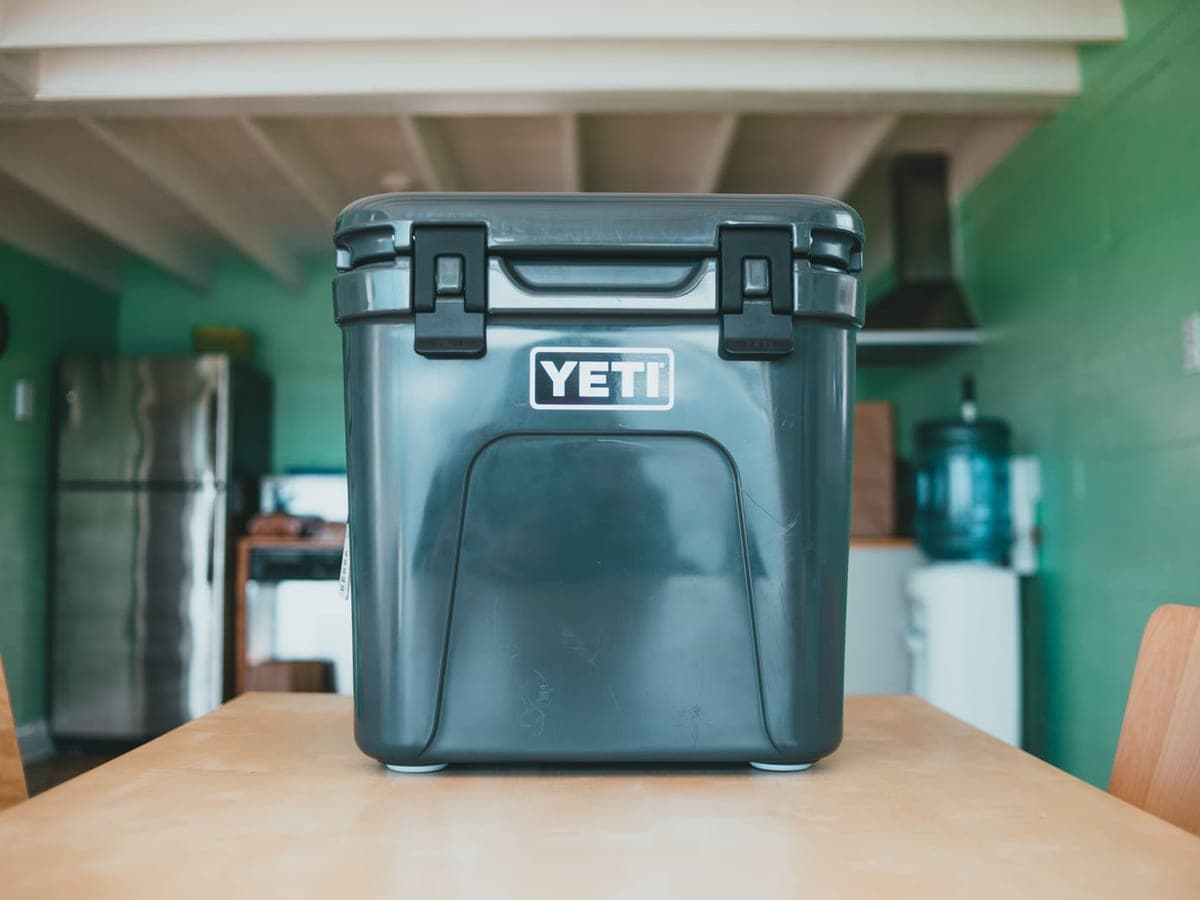 A dark gray rotomolded hard cooler with two rubber latches sitting on a wooden table — Chill & Chest, coolers, tumblers & drinkware