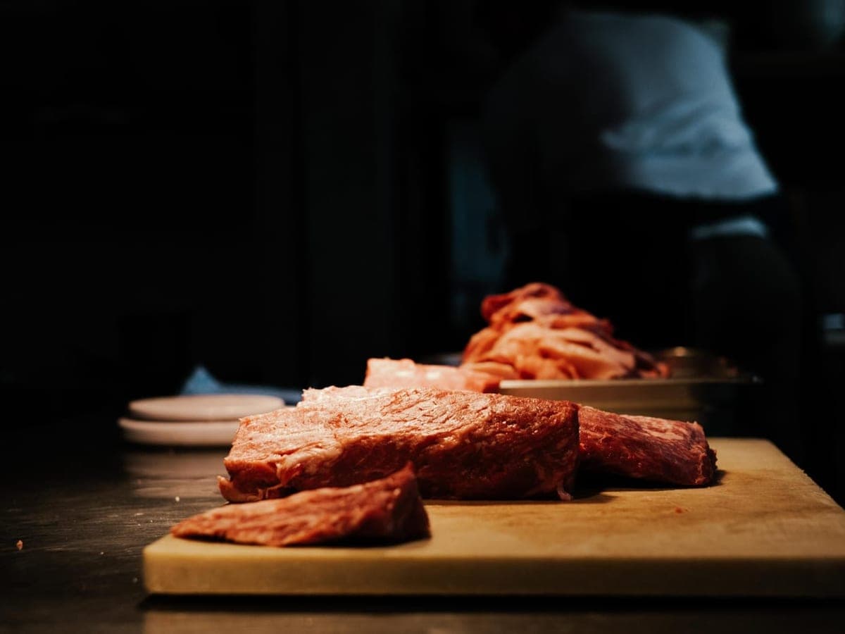 Cuts of raw meat on a wooden cutting board in a dim butcher's kitchen — Grind & Cure, meat & game processing gear