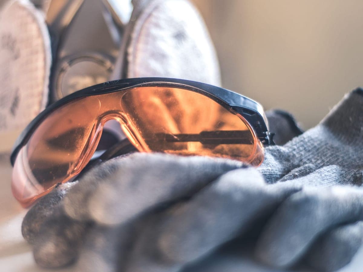 Orange-tinted shooting glasses resting on grey work gloves, with ear muffs behind — Lens & Lead, shooting & safety eyewear