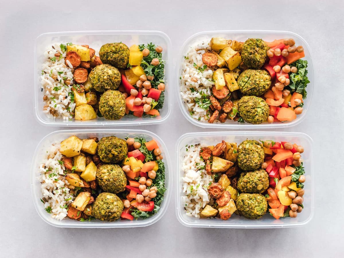 Four plastic meal prep containers packed with rice, falafel, roasted vegetables and chickpeas, seen from above — Meal & Macro, meal prep containers & lunch gear
