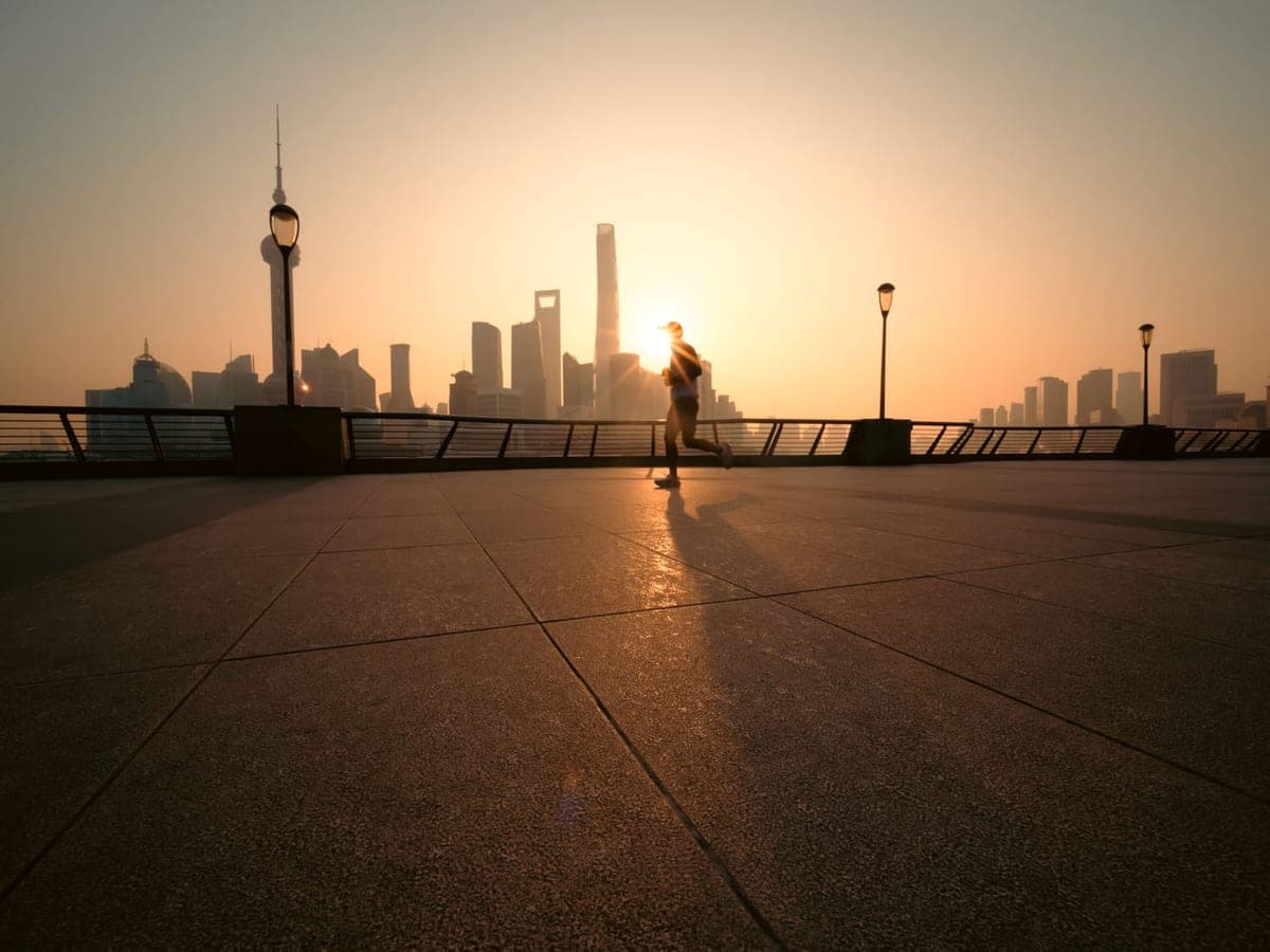 A runner silhouetted against a city skyline at sunrise — Pace & Pavement, running shoes & gear