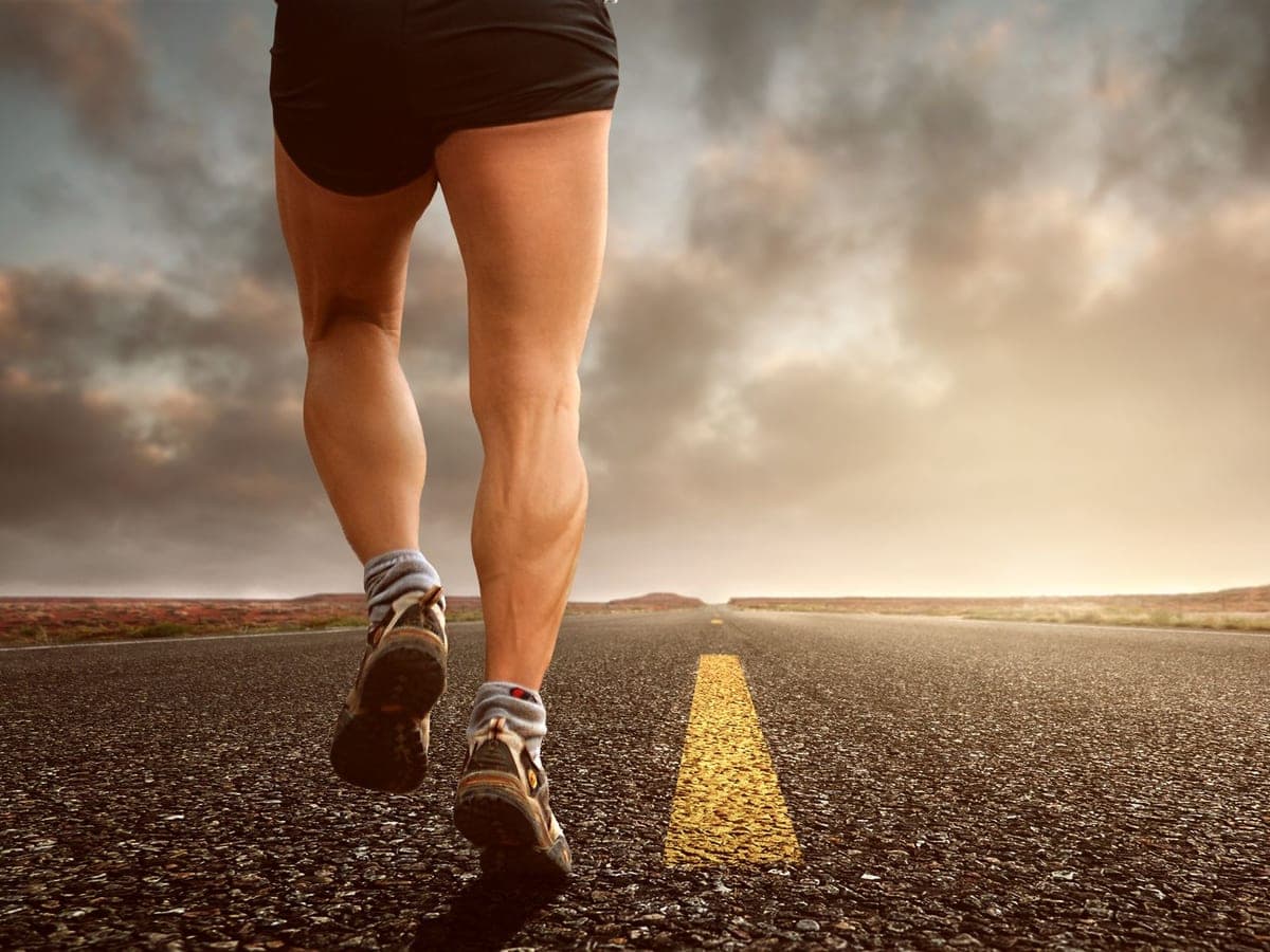 A runner's legs mid-stride on an open road at sunset — Pace & Pavement, running shoes & gear