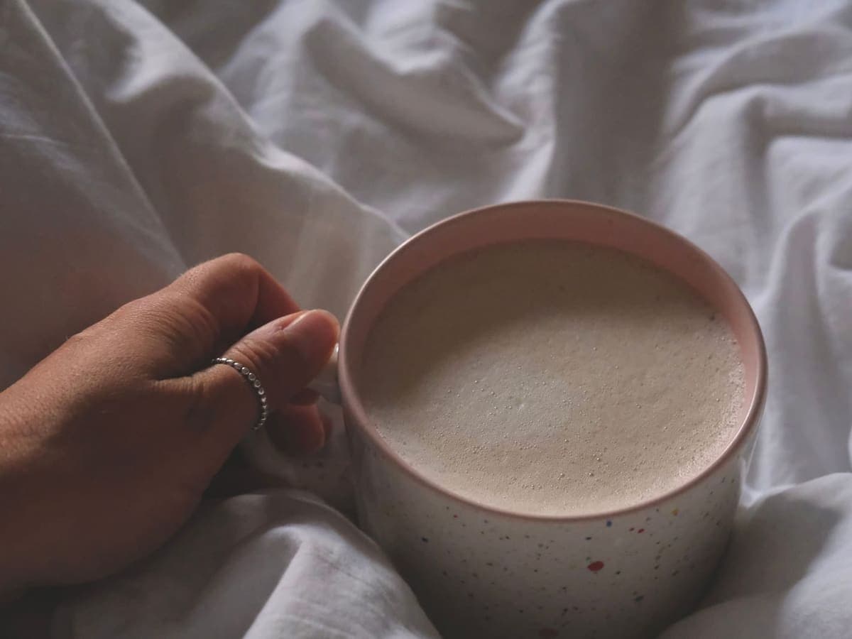 A hand wearing a slim ring holding a mug of coffee in bed — Ring & Rest, smart rings & sleep wearables