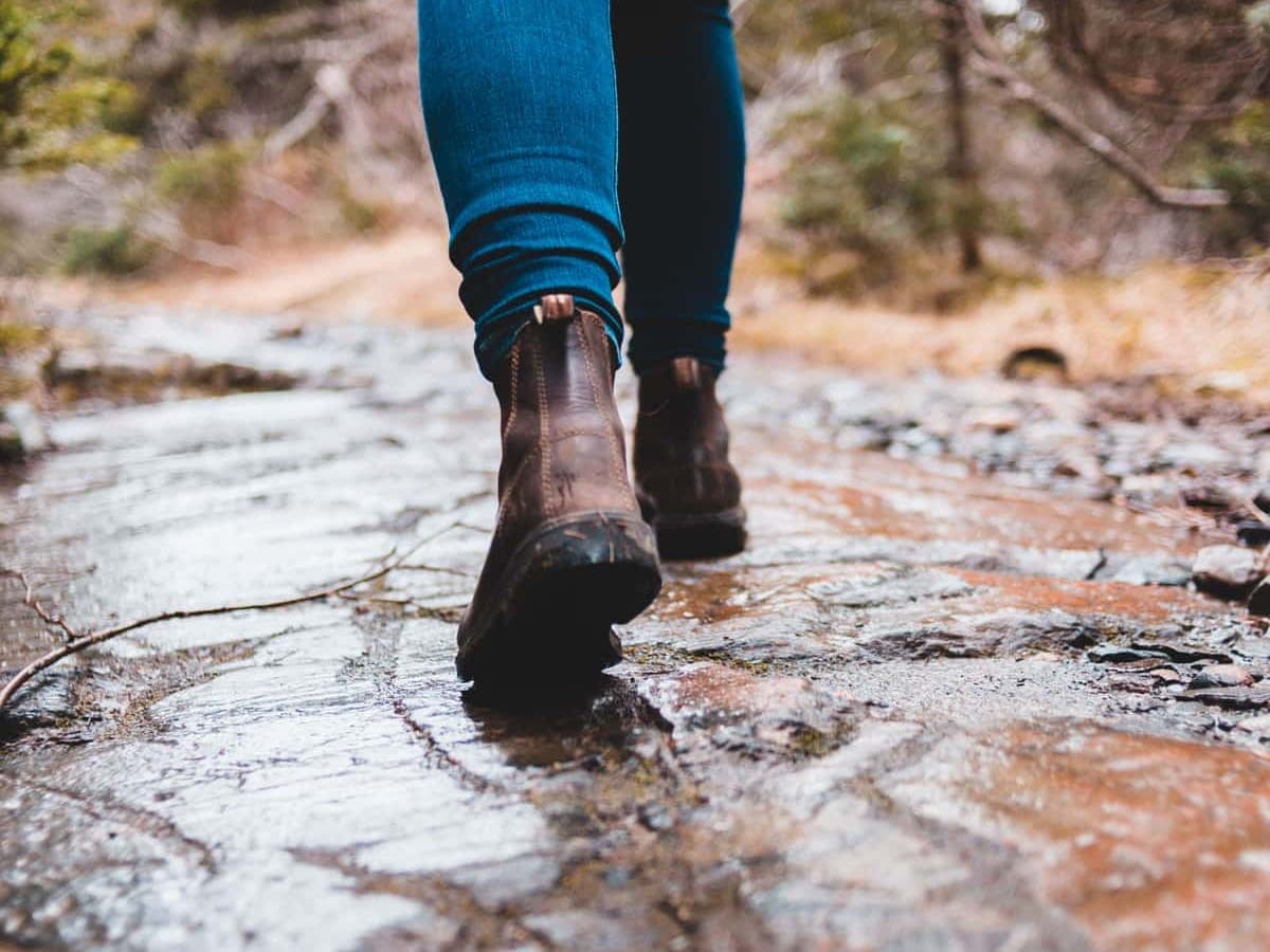 A hiker's leather boots stepping across wet rock on a forest trail — Sole & Summit, hiking boots & trail footwear