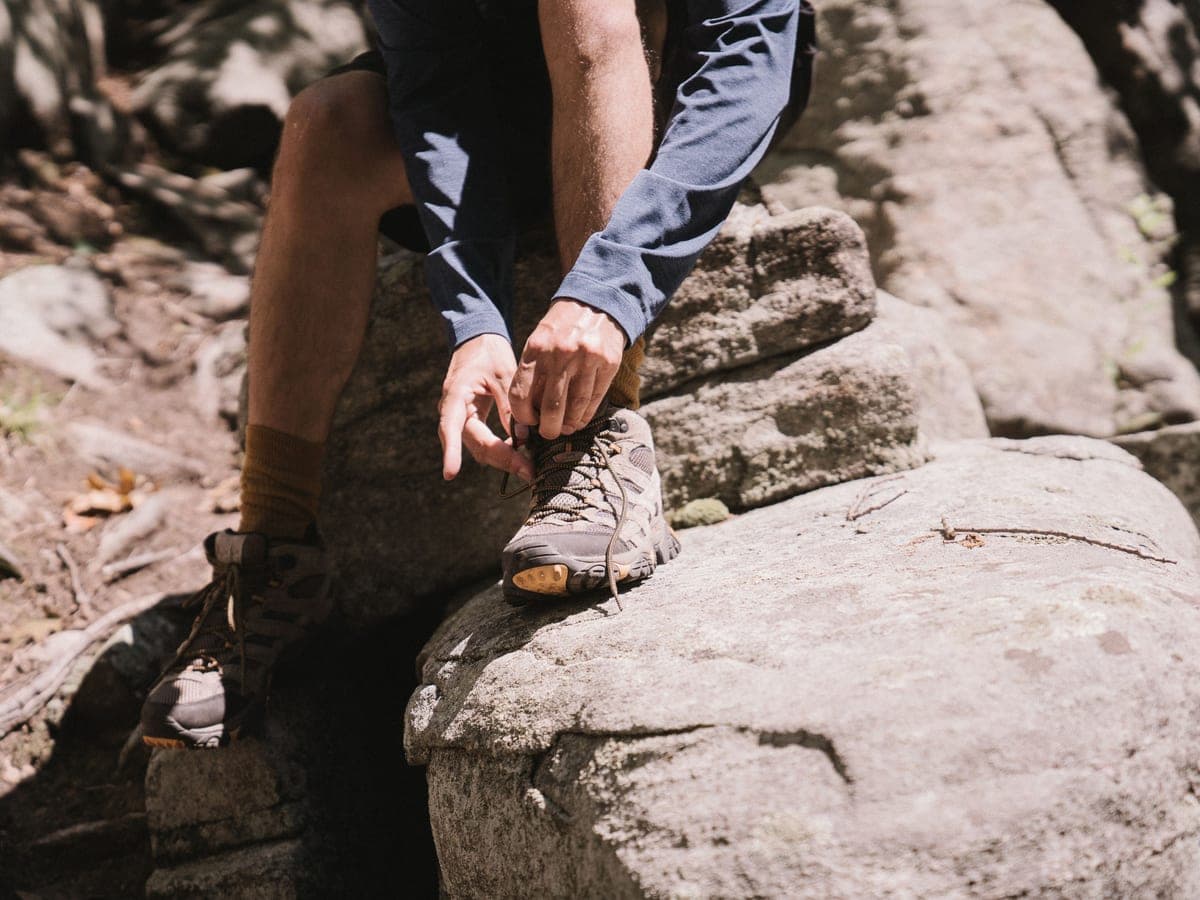 Hands lacing a hiking boot on a rocky trail